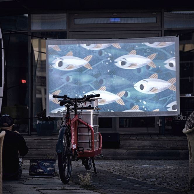 Leinwand mit animierten Fischen, projiziert von einem Lastenrad-Kino.