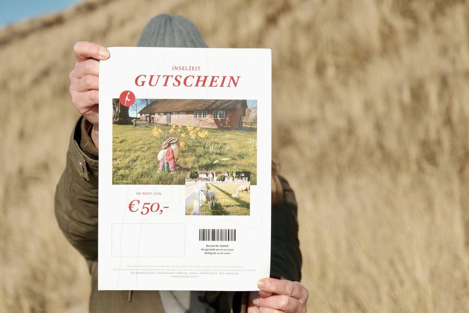 Hand hält Inselzeit-Gutschein vor Dünen