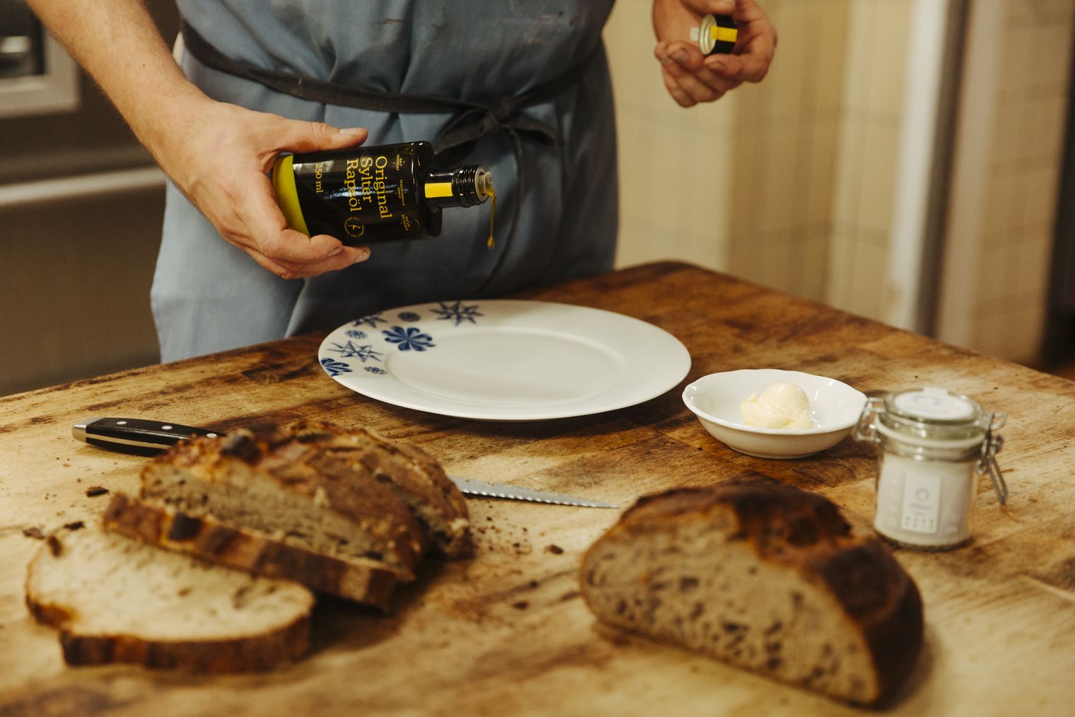 Person gießt Sylter Rapsöl auf Teller neben Brot, Butter und Salz