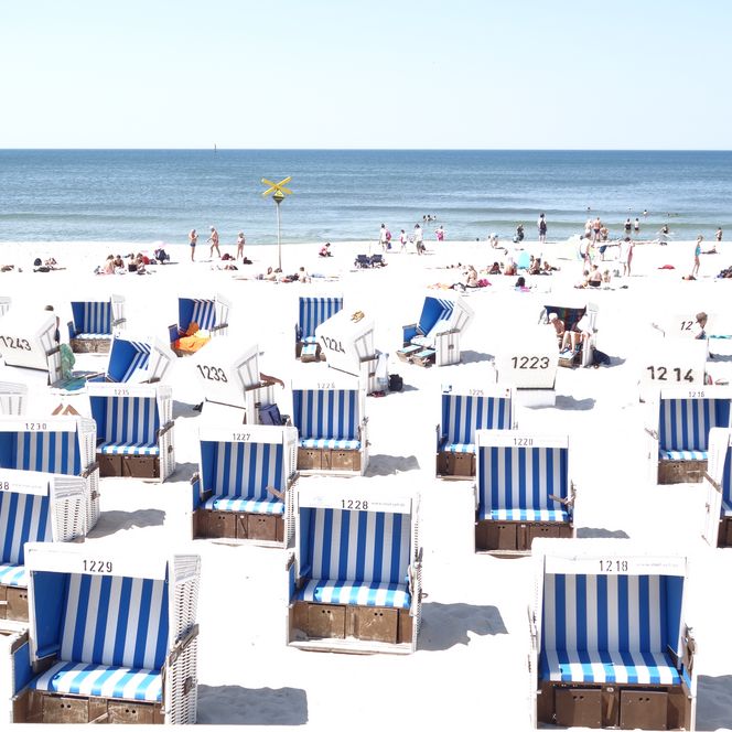 Strandkörbe in Blau-Weiß am Strand von Westerland, viele Menschen genießen Sonne und Meer.