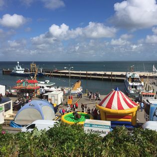 Hafenfest in Hörnum mit Ständen, Hüpfburg, Karussellzelt und Schiffen am Kai.