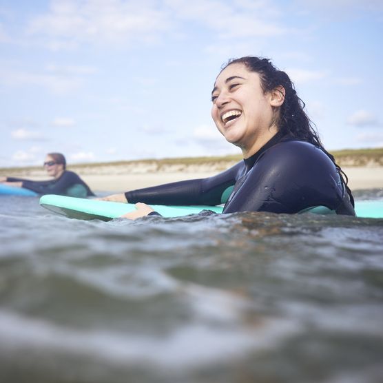Junge Frau lacht im Neoprenanzug auf Surfbrett im Wasser.