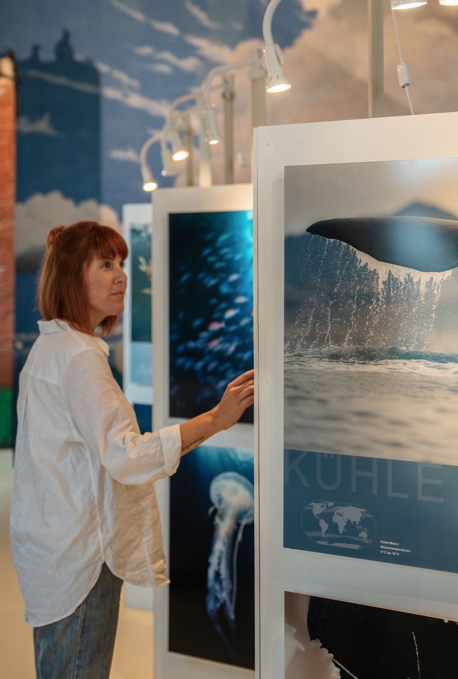 Frau betrachtet ein Bild eines Walschwanzes in einer beleuchteten Ausstellung mit maritimen Motiven.