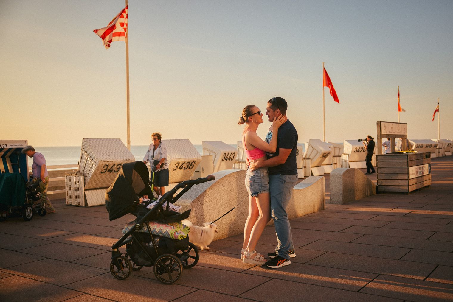 Paar umarmt sich an Promenade im Abendlicht mit Kinderwagen.