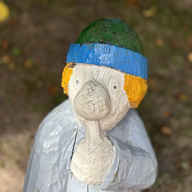 Holzfigur mit Finger vor dem Mund, grüne Mütze und orange Haare.