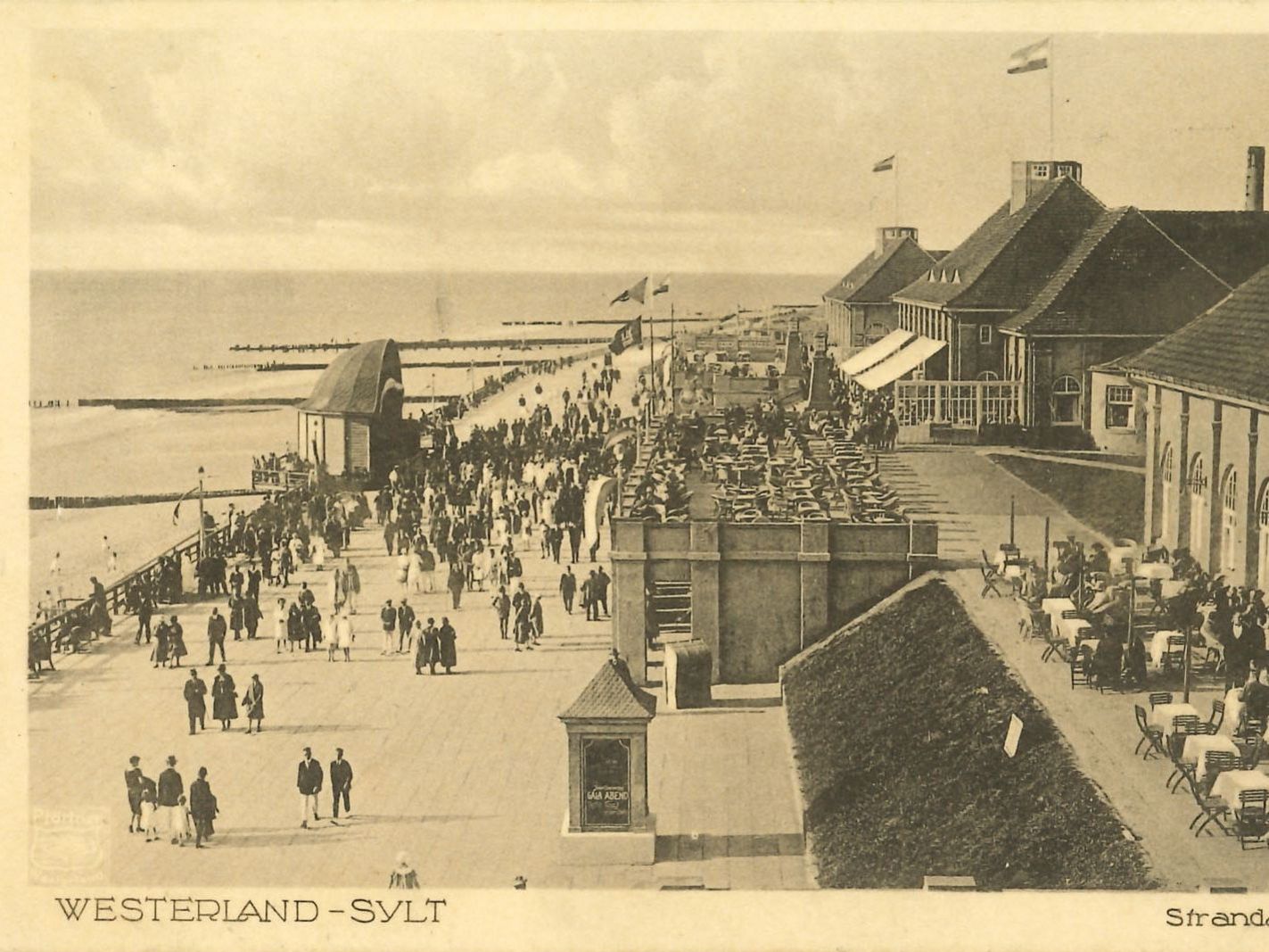Historische Strandpromenade Westerlands mit vielen Spaziergängern und Gebäuden am Meer.
