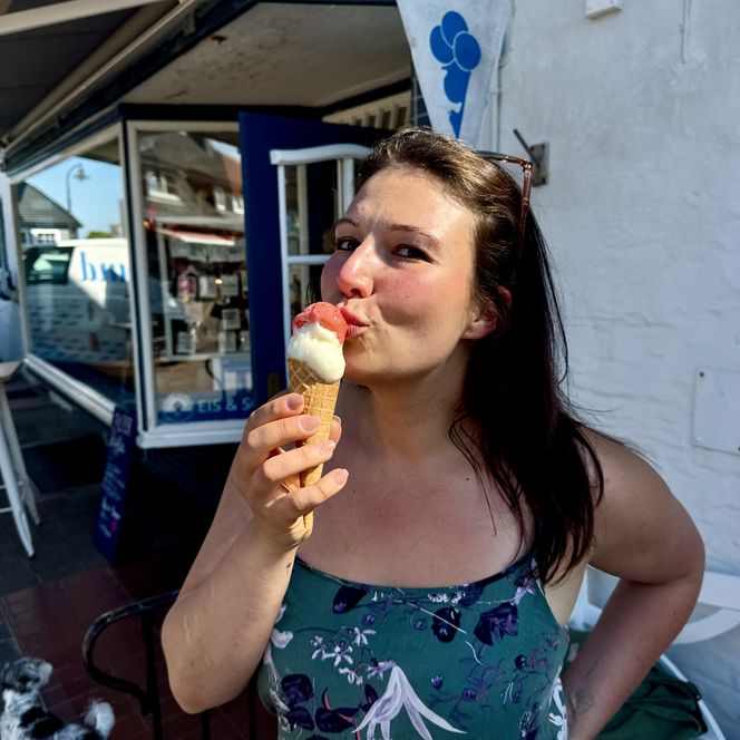 Frau isst ein zweikugeliges Eis in einer Waffel vor einer Eisdiele.