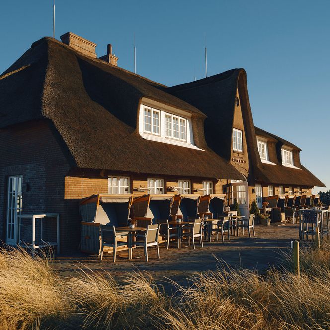 Reetgedecktes Hotel mit Terrasse und Strandkörben in den Dünen