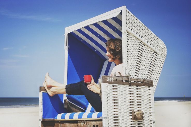 Frau sitzt im Strandkorb mit Kaffeetasse in der Hand