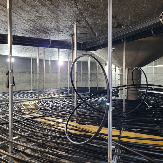 Schwarze Kunststoffrohre in dichten Schlaufen auf Metallgestell im Eisspeicher-Innenraum.