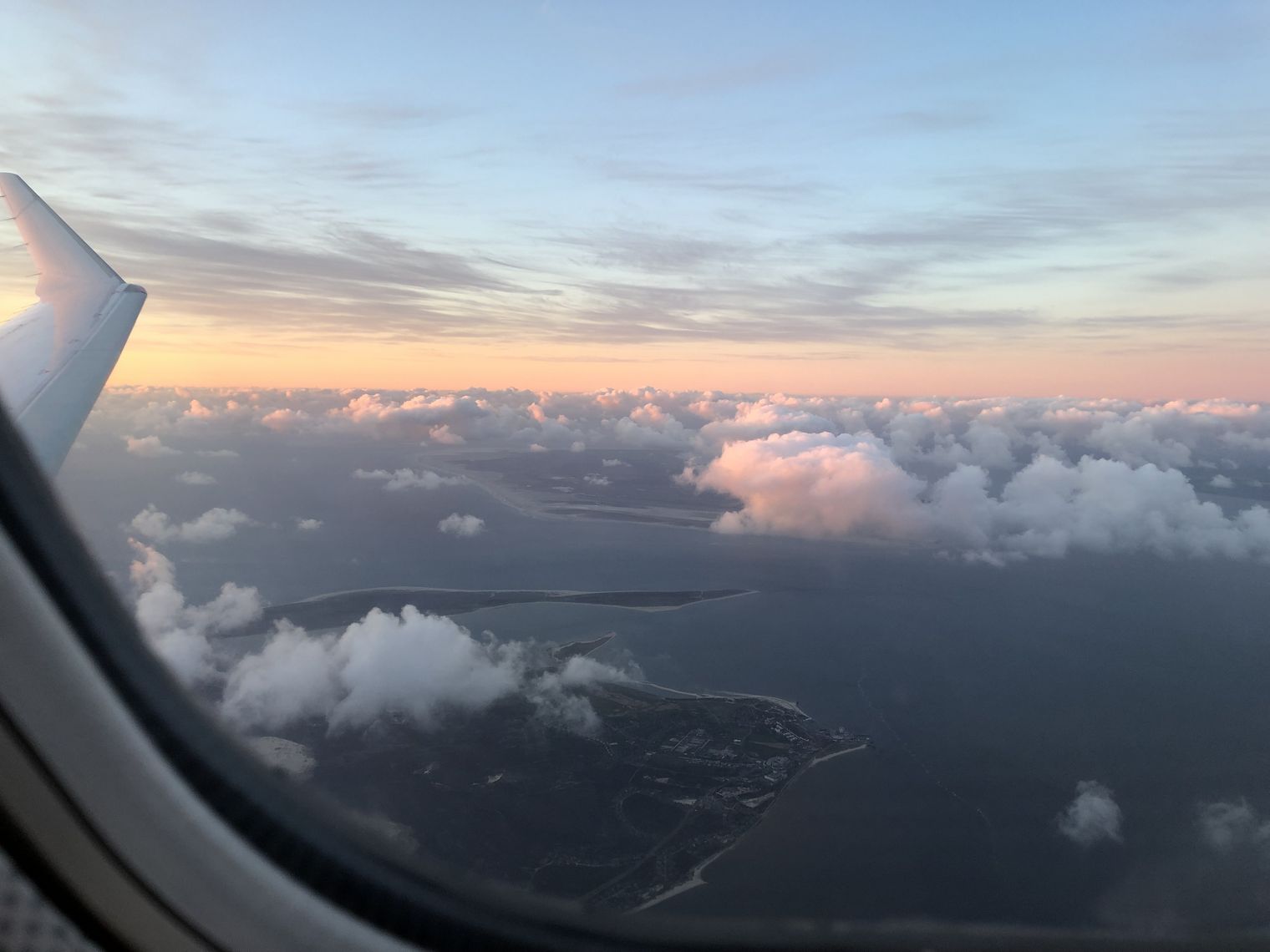 Luftaufnahme der Küste von Sylt mit dem Ellenbogen, Wanderdünen und der benachbarten Insel Rømø, mit Wolken im warmen Licht eines Sonnenuntergangs oder -aufgangs.