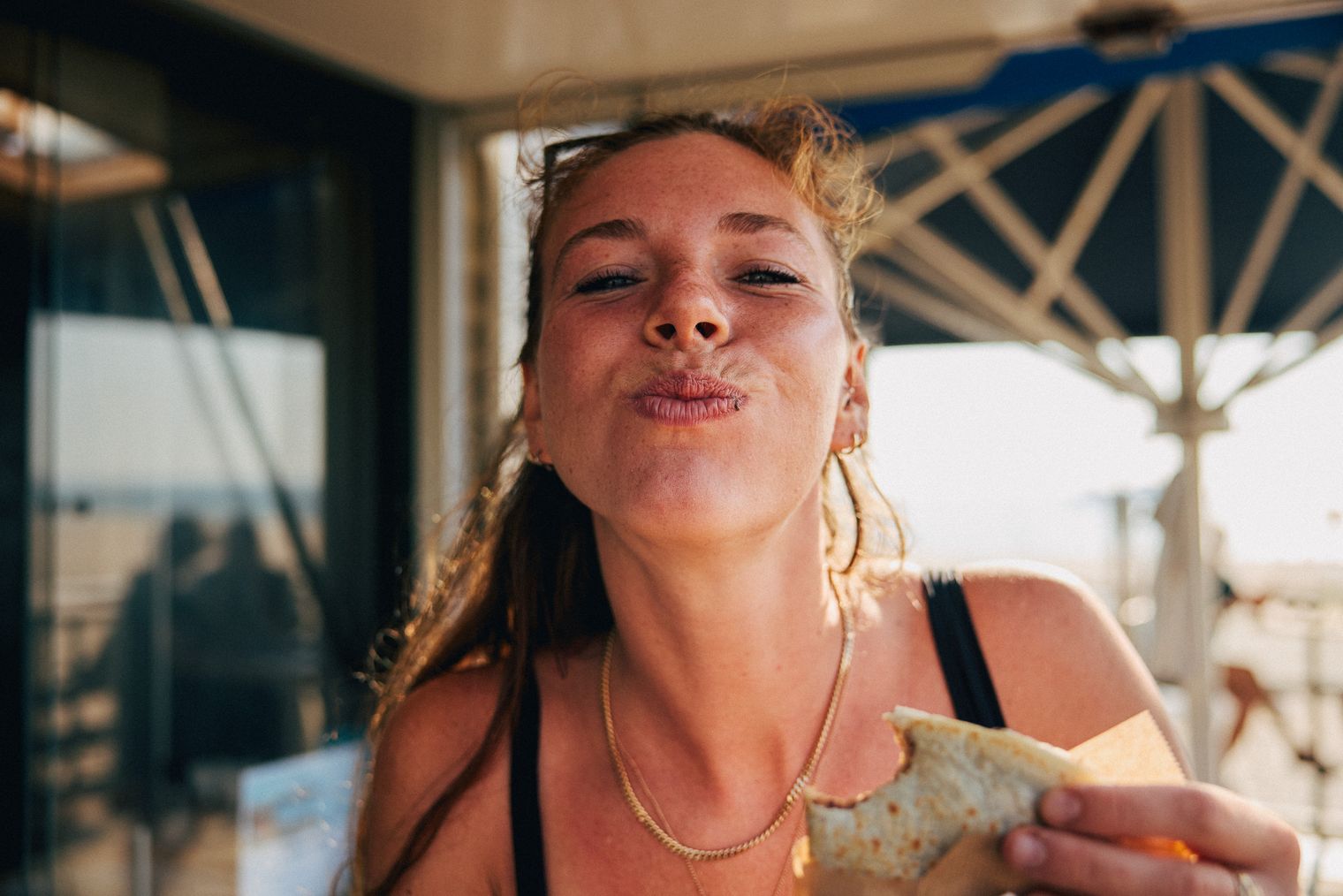 Donna in abiti estivi che gusta uno spuntino davanti all'ombrellone e alla spiaggia.