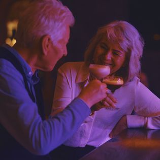 Älteres Paar an einer Bar stößt lächelnd mit eleganten Cocktails an.
