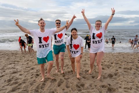 Vier junge Menschen in T-Shirts mit der Aufschrift "I love Sylt" ausgelassen am Strand