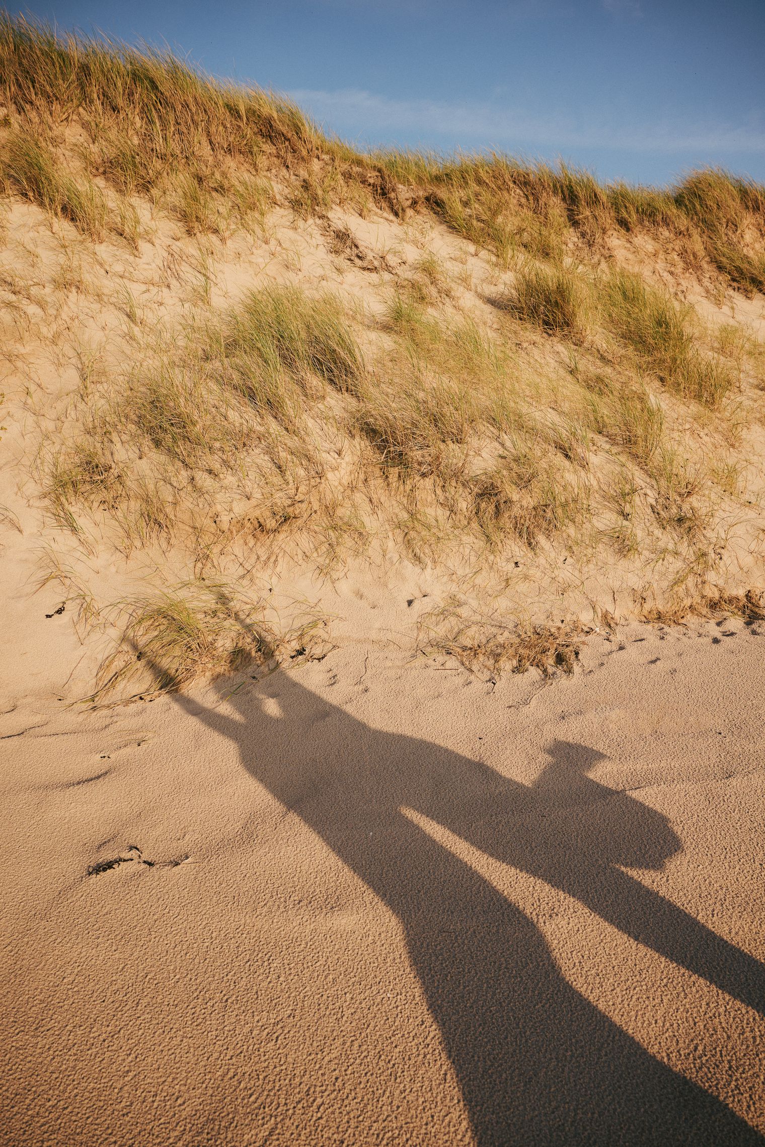 Schatten einer Person mit Kamera vor Sylter Dünenlandschaft im Sonnenlicht.