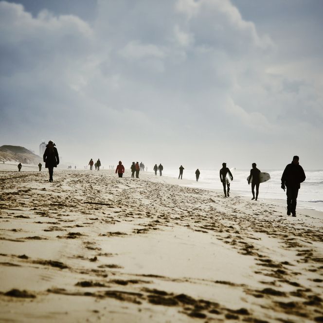Winterlicher Strandspaziergang auf Sylt Menschen spazieren und surfen an einem winterlichen Strand auf Sylt.