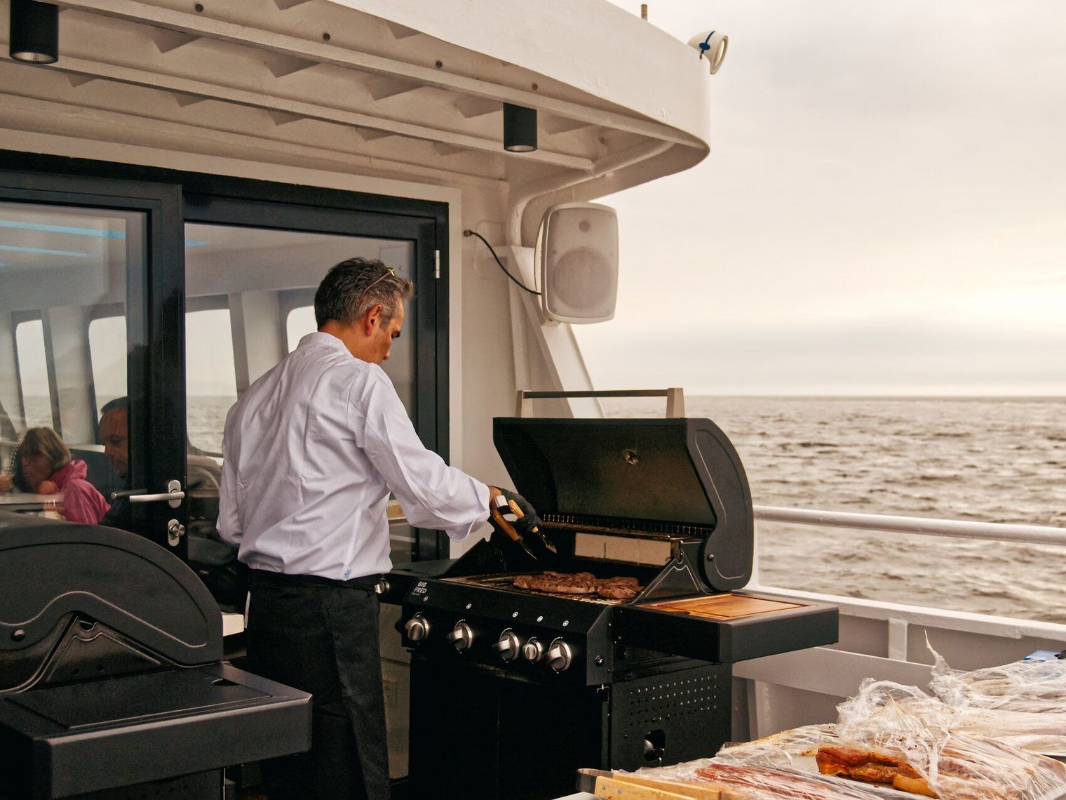 Mann grillt auf Schiff mit Meerblick