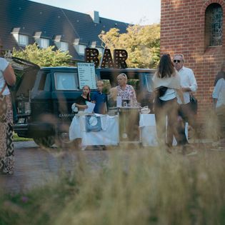 Menschen stehen an mobiler Festivalbar im Freien.