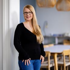 Blonde Frau mit Brille steht lächelnd im modernen Büro