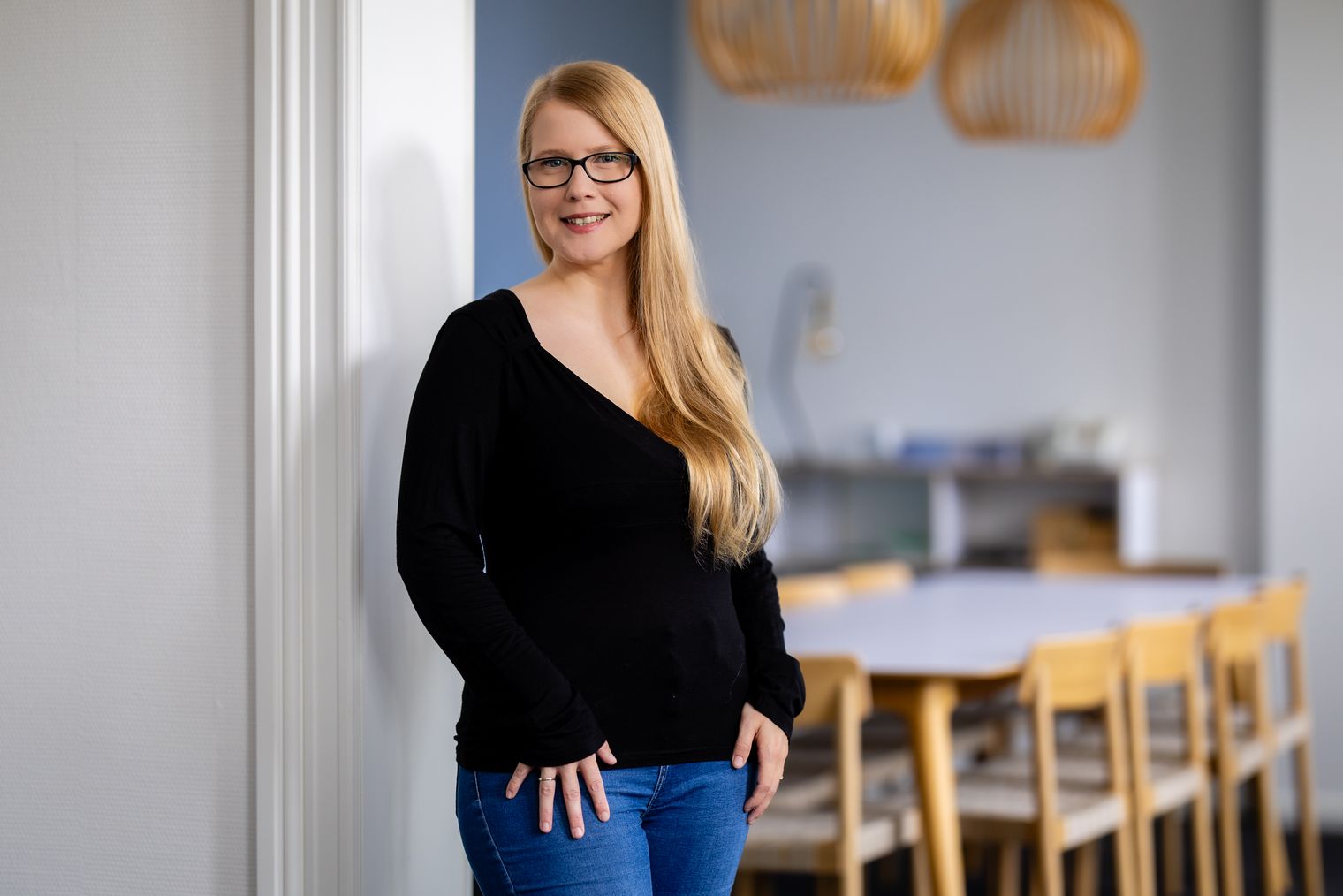 Blonde Frau mit Brille steht lächelnd im modernen Büro