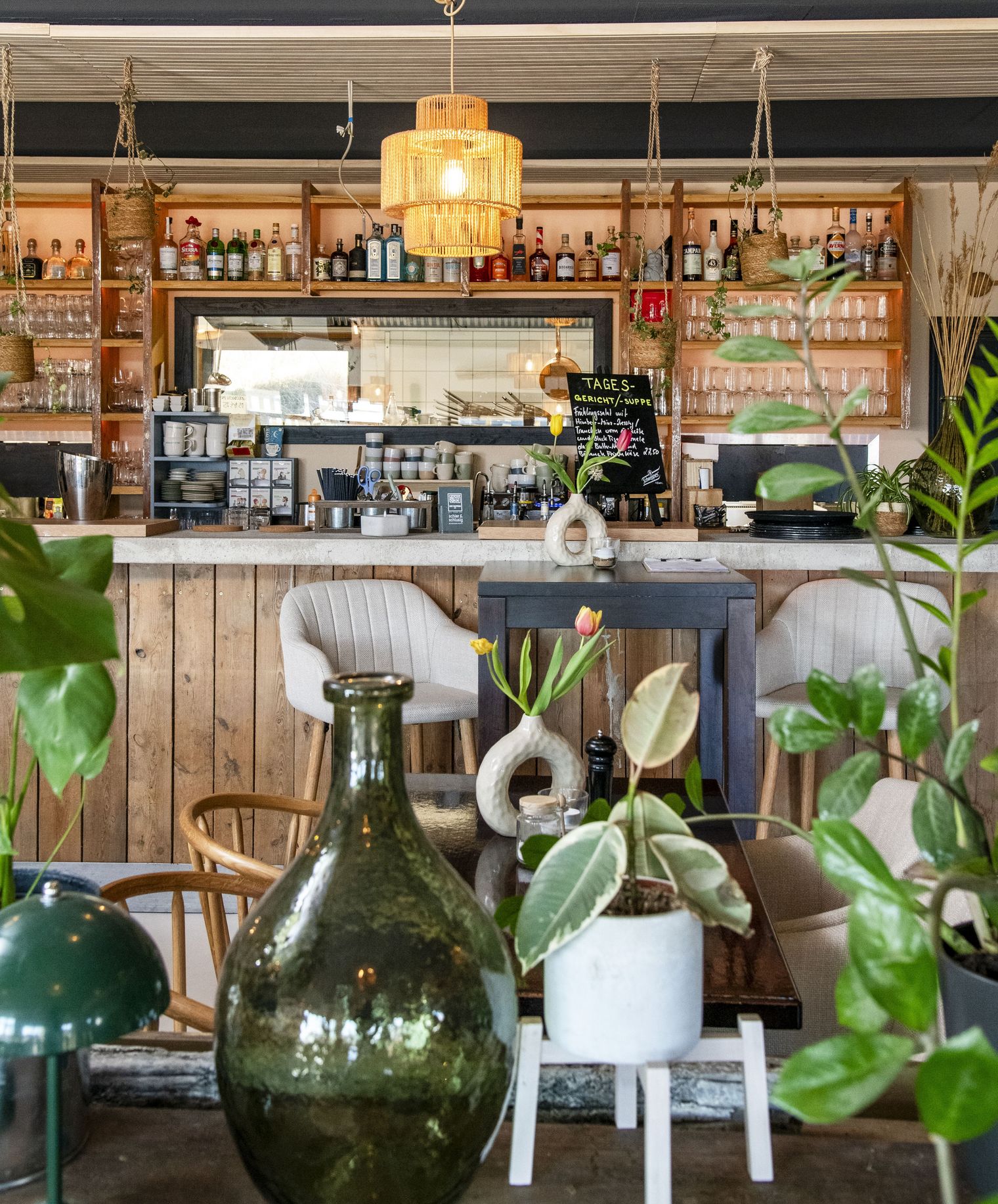 Tresen aus Holz mit Pflanzen, Flaschenregalen und Lampen im Café Klapprad in Wenningstedt.
