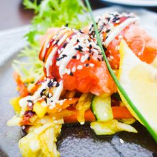 Lachs mit Sesam, Gemüse und Zitrone auf Glasplatte angerichtet.