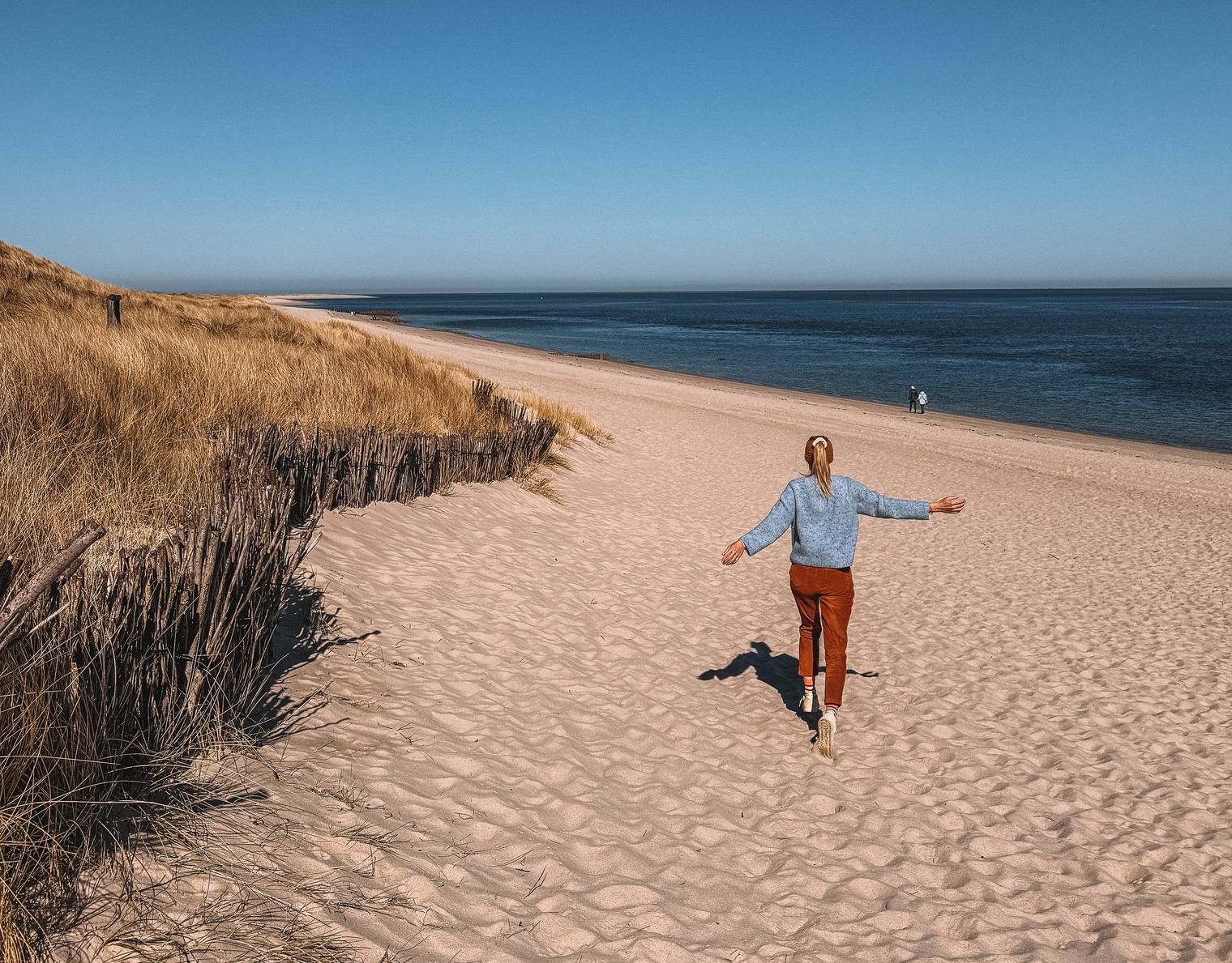 Person läuft mit ausgebreiteten Armen am Sandstrand entlang.