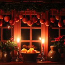 Weihnachtlich dekoriertes Fenster mit hängenden roten Äpfeln, Kerzen und Töpfen mit weihnachtlichen Dekorationen.
