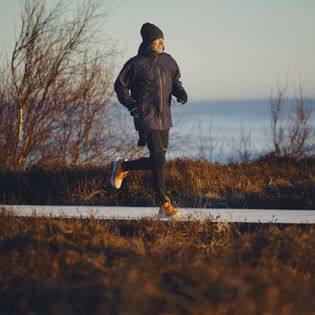 Mann joggt bei Morgensonne auf Holzweg durch Heidelandschaft an der Küste