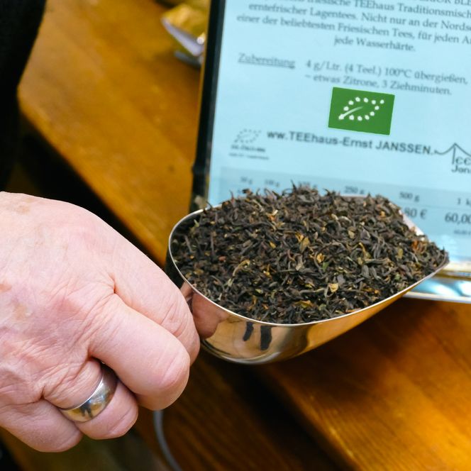 Hand hält Metallschaufel mit losem schwarzen Tee.