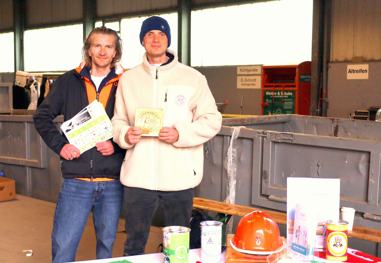 Zwei Männer präsentieren Informationsmaterial bei einer Flohmarkt- und Spendenaktion