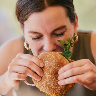 Frau beißt in einen Burger mit Sesambrötchen und Salat im Twisters in Wenningstedt.