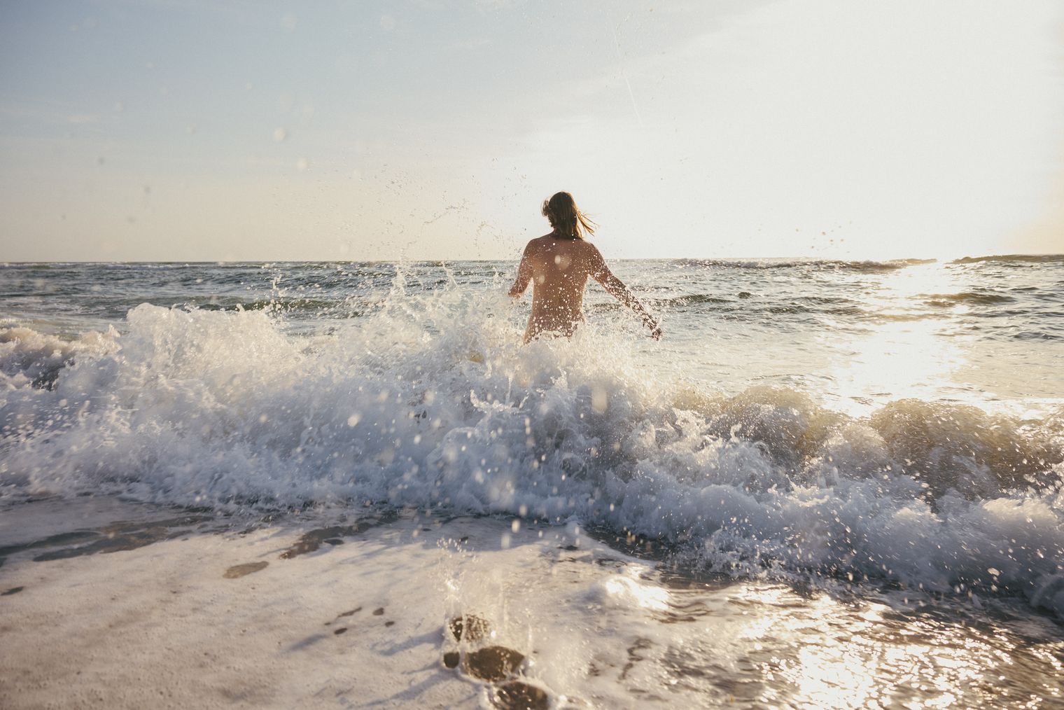 Person läuft bei Sonnenuntergang in die Nordseewellen