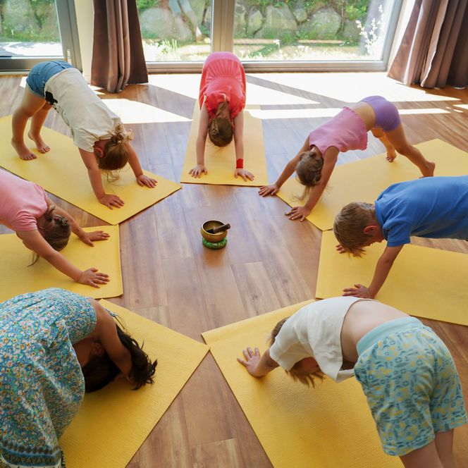 Kinder in der Yoga Pose Herabschauender Hund auf gelben Matten