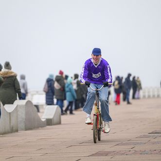 Teilnehmer mit Startnummer 193 fährt auf einem Klapprad über eine Promenade, umgeben von Zuschauern und weiteren Fahrern.