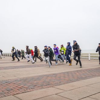 Gruppe von Läuferinnen und Läufern in warmer Kleidung auf einer Strandpromenade vor grauem Meer und Seebrücke.