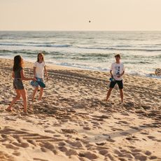 Vier Jugendliche spielen Beachball am Sandstrand bei Sonnenuntergang.