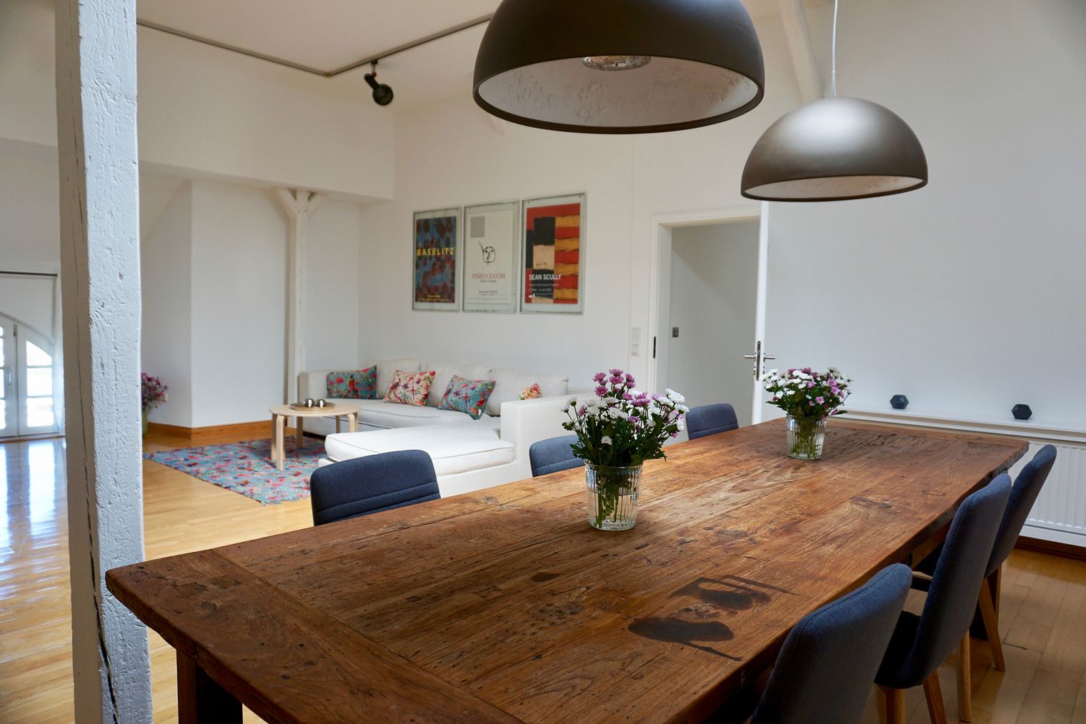 Holztisch mit Blumenvasen, gemütliche Sitzecke und Wandkunst im Wohnzimmer des Konsumvereins Keitum.