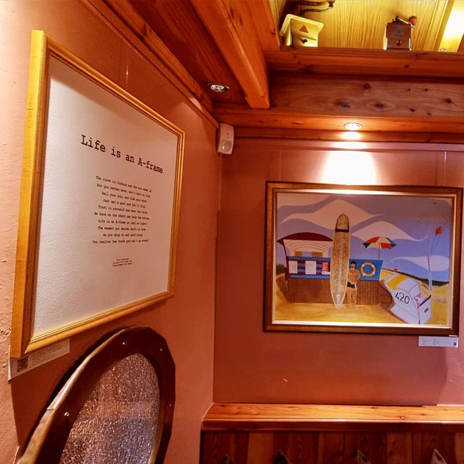 Gedicht auf Leinwand und Strandbild in einem Raum mit viel Holz und warmem Licht.