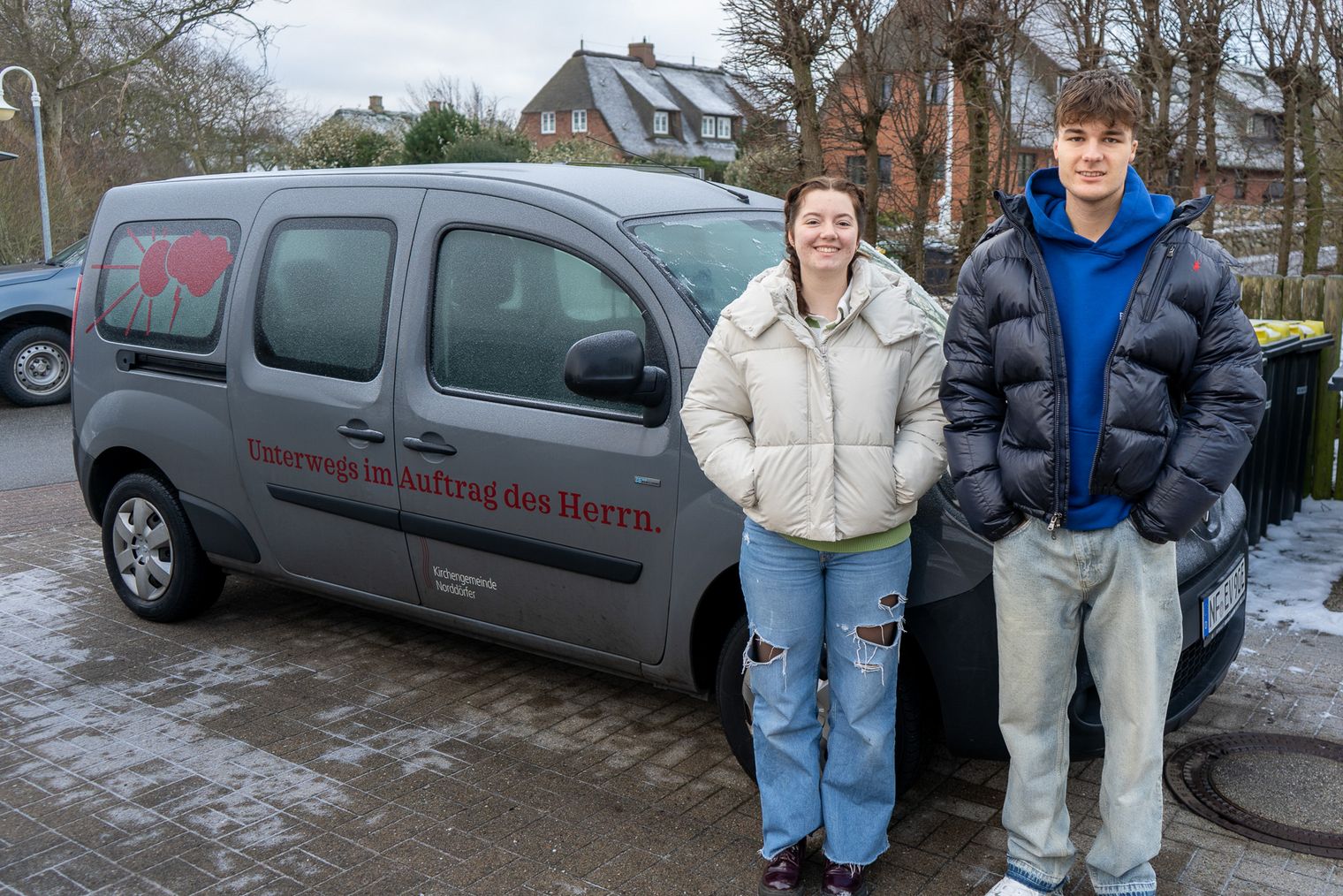 Zwei junge Menschen stehen vor dem Auto der Norddörfer Kirchengemeinde.