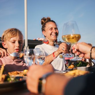 Eine Familie isst gemeinsam beim Samoa Seepferdchen. Die Mutter und ein weiterer Erwachsener stoßen mit einem Glas Wein an.