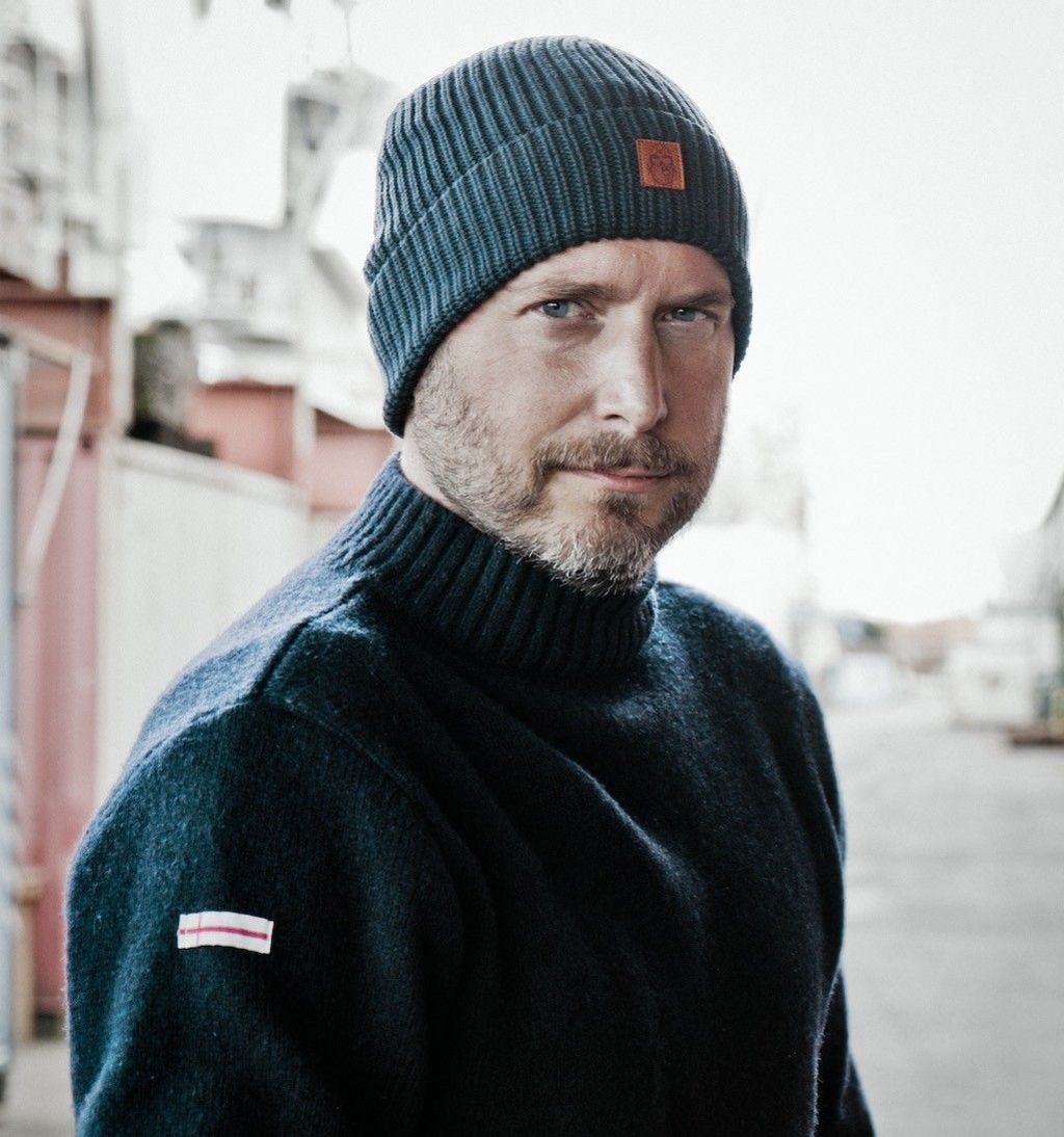 Mann mit Strickmütze und Pullover blickt ruhig in die Kamera.