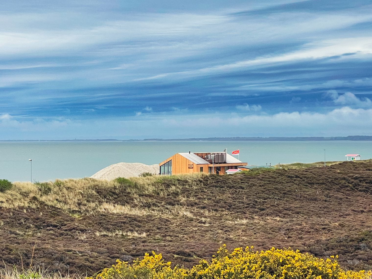 Barrierefreiheit: Alternativer Text: Haus in Dünenlandschaft mit Meerblick und wolkigem Himmel