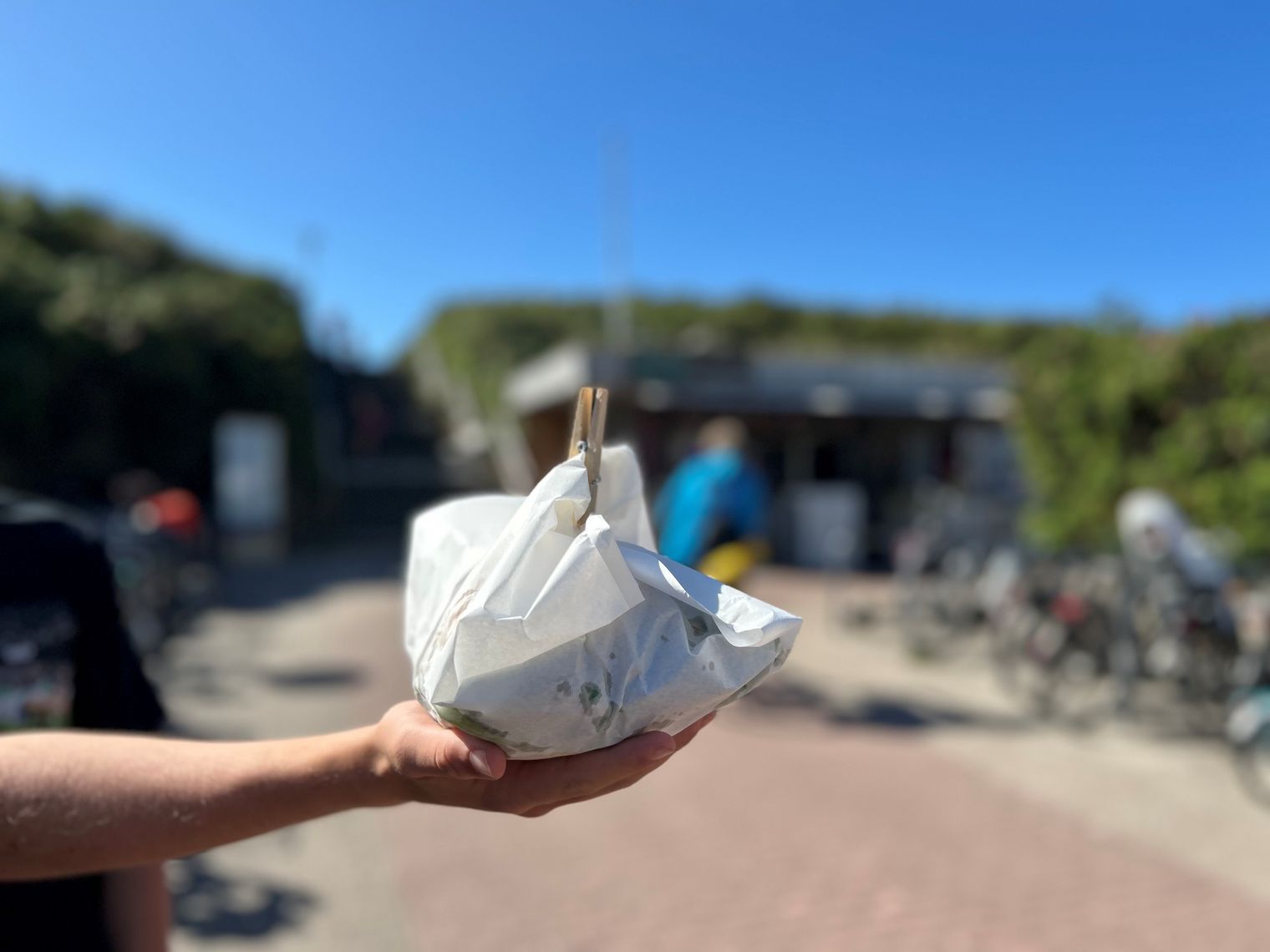 Hand hält verpacktes Gericht vor dem unscharfen Kiosk „Beach Box“.