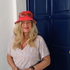 Porträt einer Frau mit rotem Sonnenhut vor blauer Tür