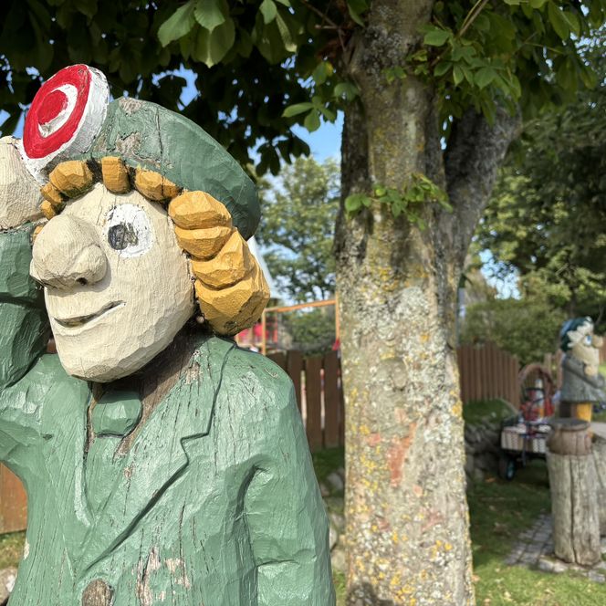 Bunte Holzfigur eines Polizisten auf Spielplatz mit Bäumen und Zaun