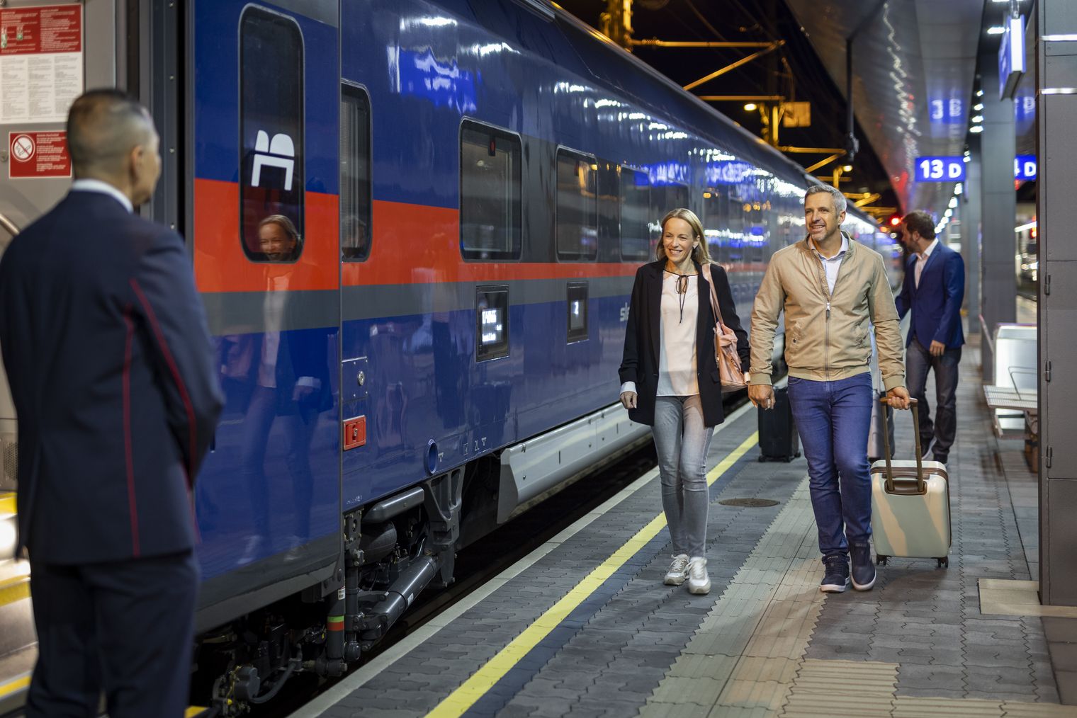 Reisende steigen nachts am Bahnsteig aus einem modernen Zug.