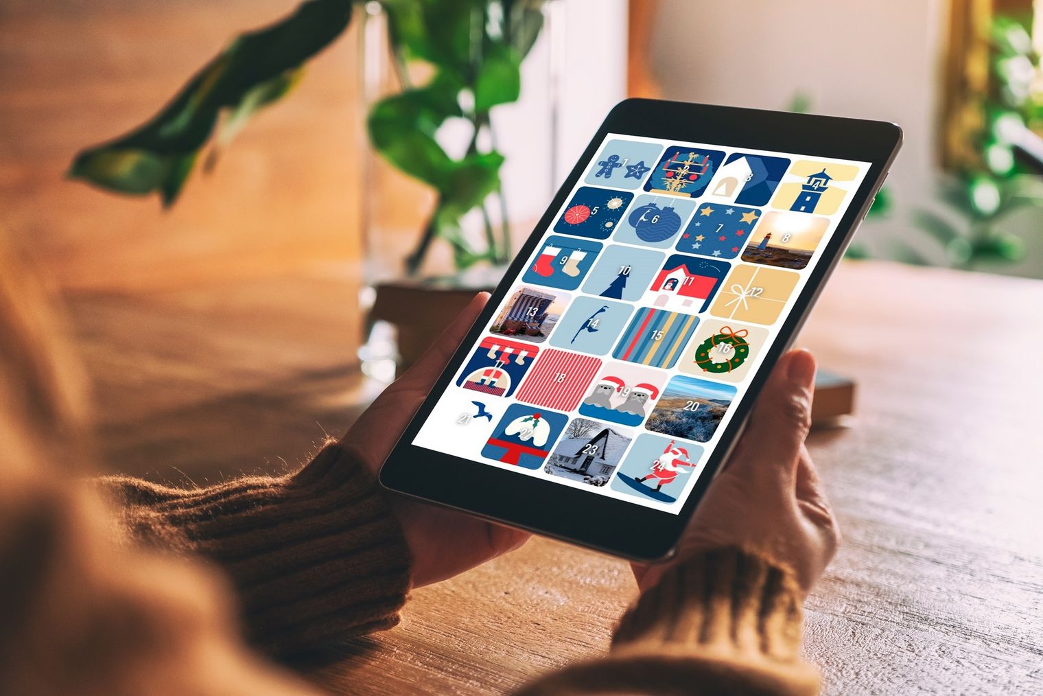Hände halten ein Tablet mit 24 nummerierten Türchen eines digitalen Adventskalenders.