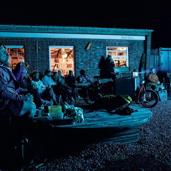 Menschen schauen bei Nacht draußen gemeinsam einen Film vor einem Gebäude.
