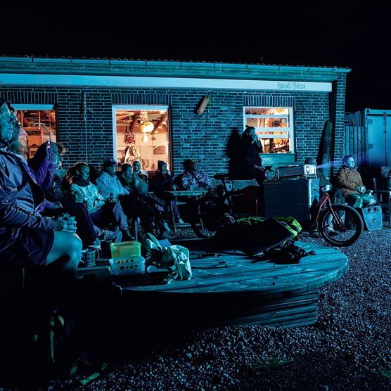 Menschen schauen bei Nacht draußen gemeinsam einen Film vor einem Gebäude.